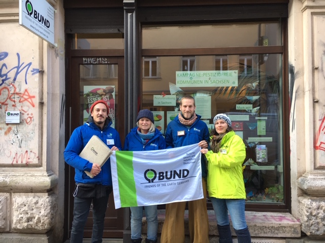 Vier Menschen stehen vor dem Büro des BUND Dresden und halten eine Fahne des BUND.